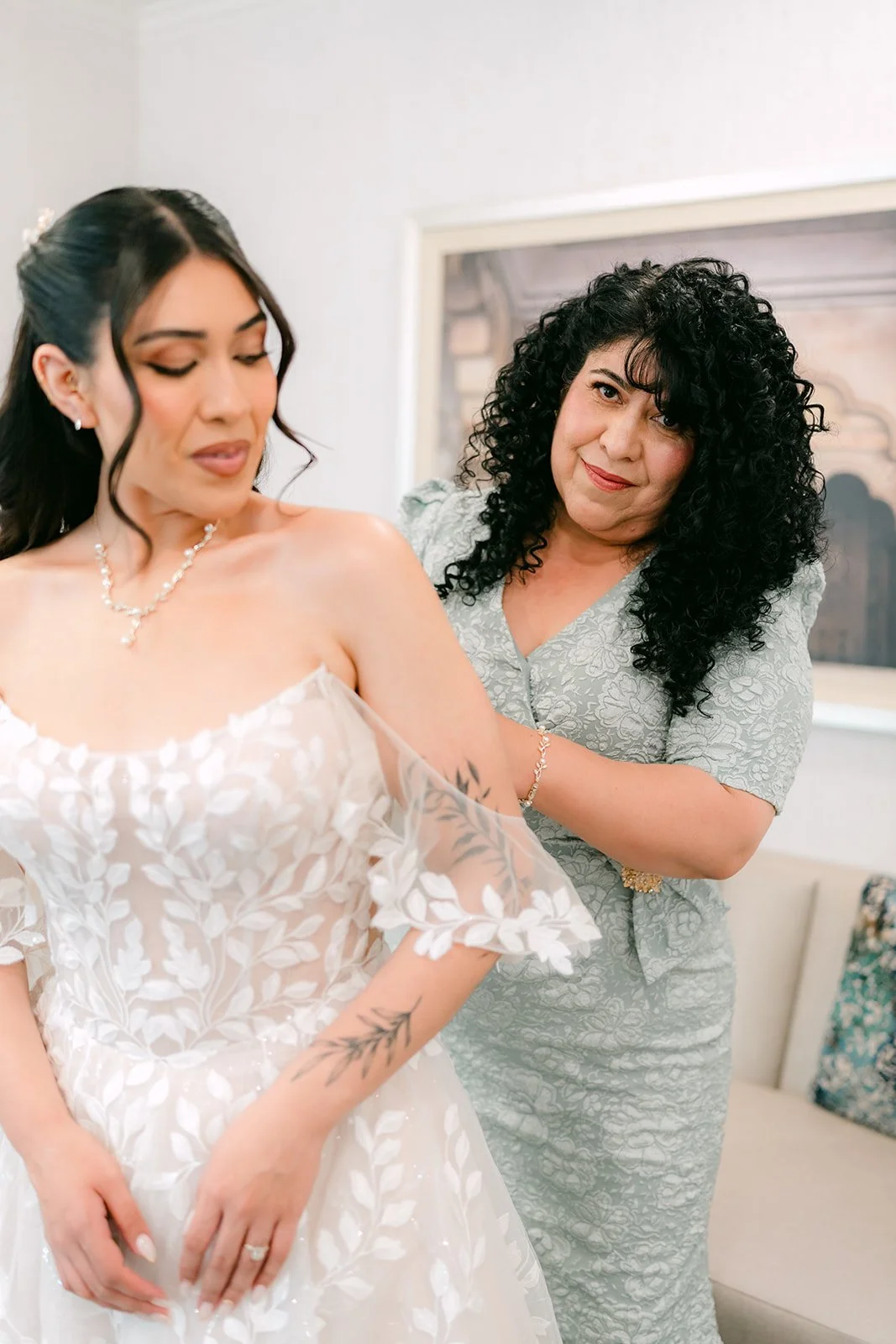 Fernanda and a bridesmaid sharing a laugh as she finishes getting dressed.