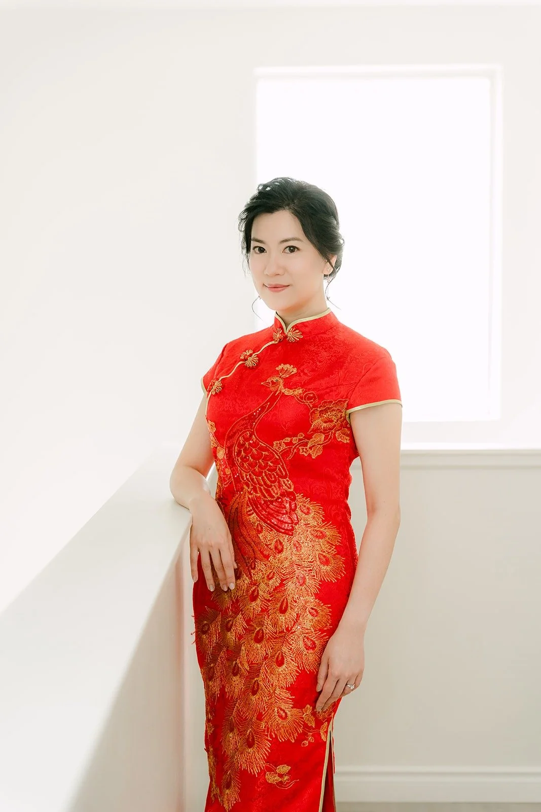Eunice in her red and gold qipao standing by a bright window