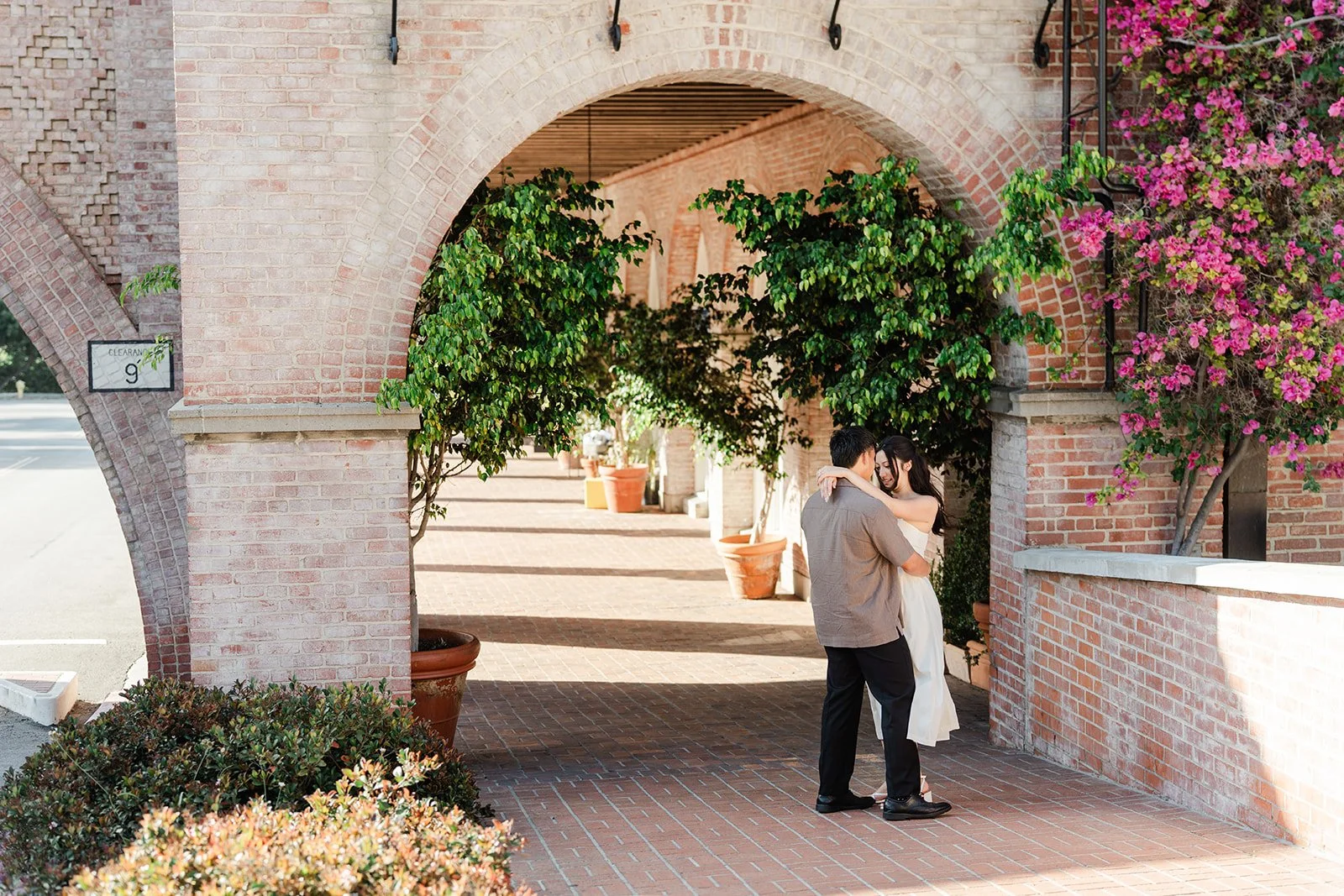 Victoria and Andrew walk through a brick archway framed by greenery at Malaga Cove Plaza.