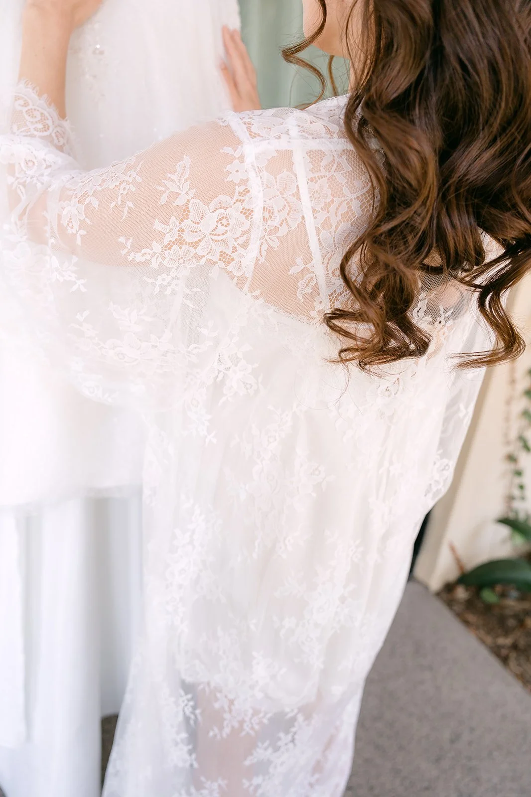 Soft curls cascading over the lace robe as the bride admires her gown