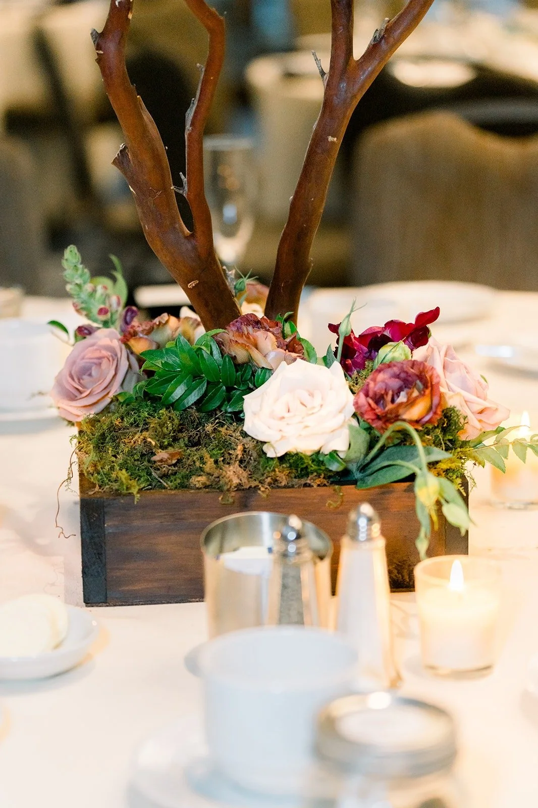 A wooden box centerpiece with burgundy and blush flowers and candles