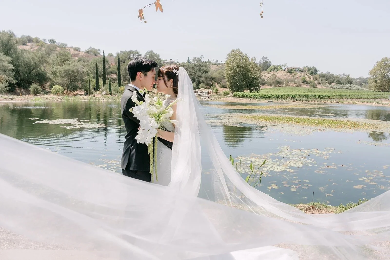 Marina and Tyler kissing by the lake at Monte Bella as her long veil sweeps across the grass