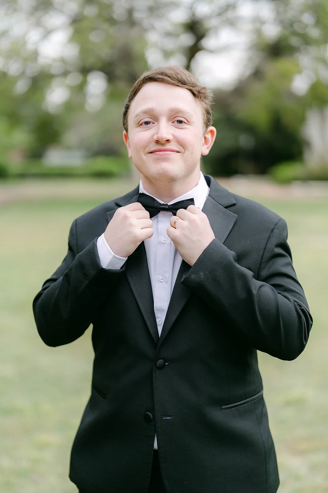 Matthew adjusting his bow tie on the lawn, photographed by One and Only Production