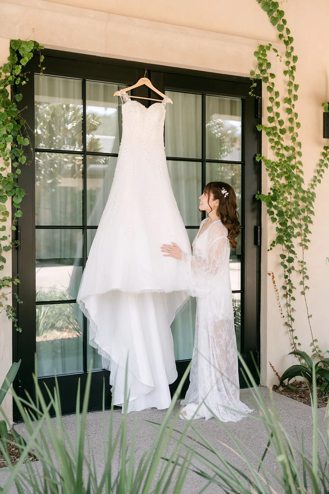Marina in a lace robe beside her wedding gown hanging in the bridal suite doorway