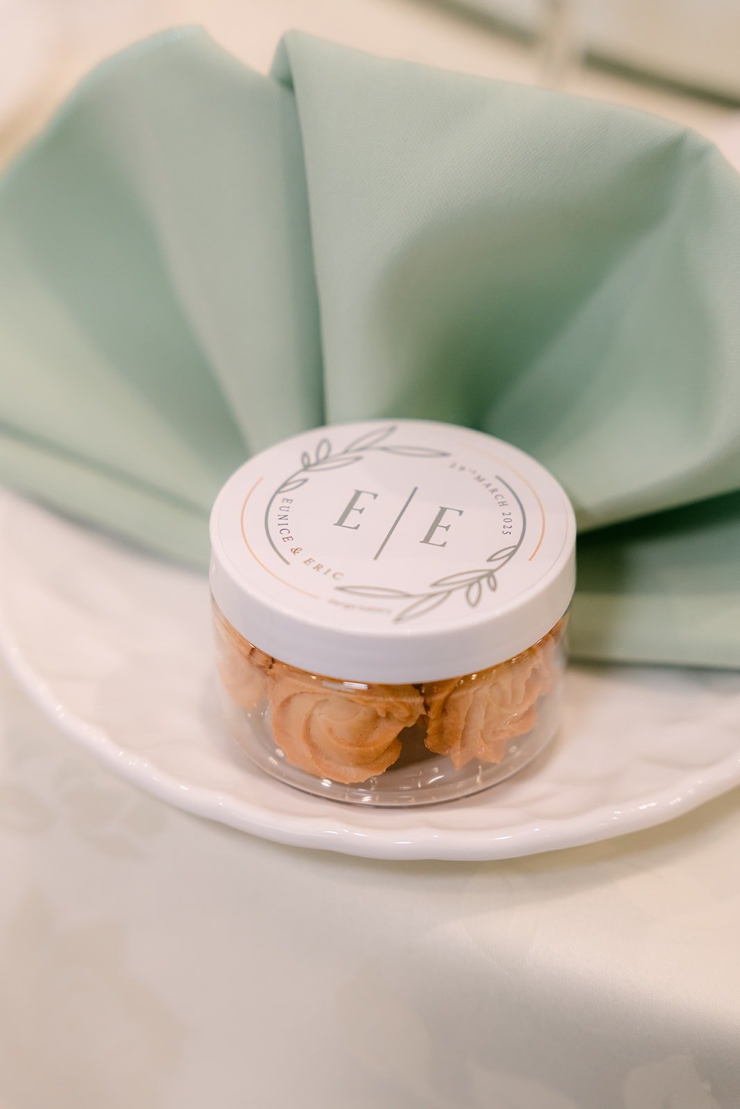 A wedding favor jar marked E and E on a sage green napkin
