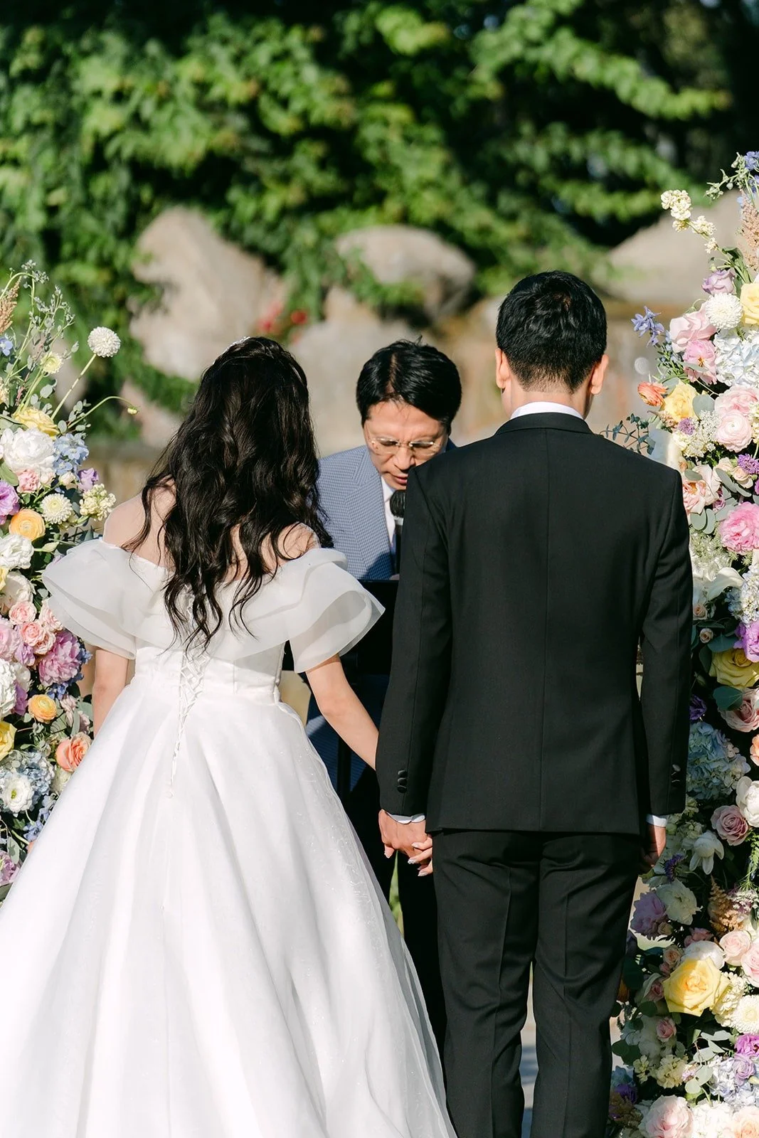 Jeannie and Eunsang facing their pastor under the floral columns