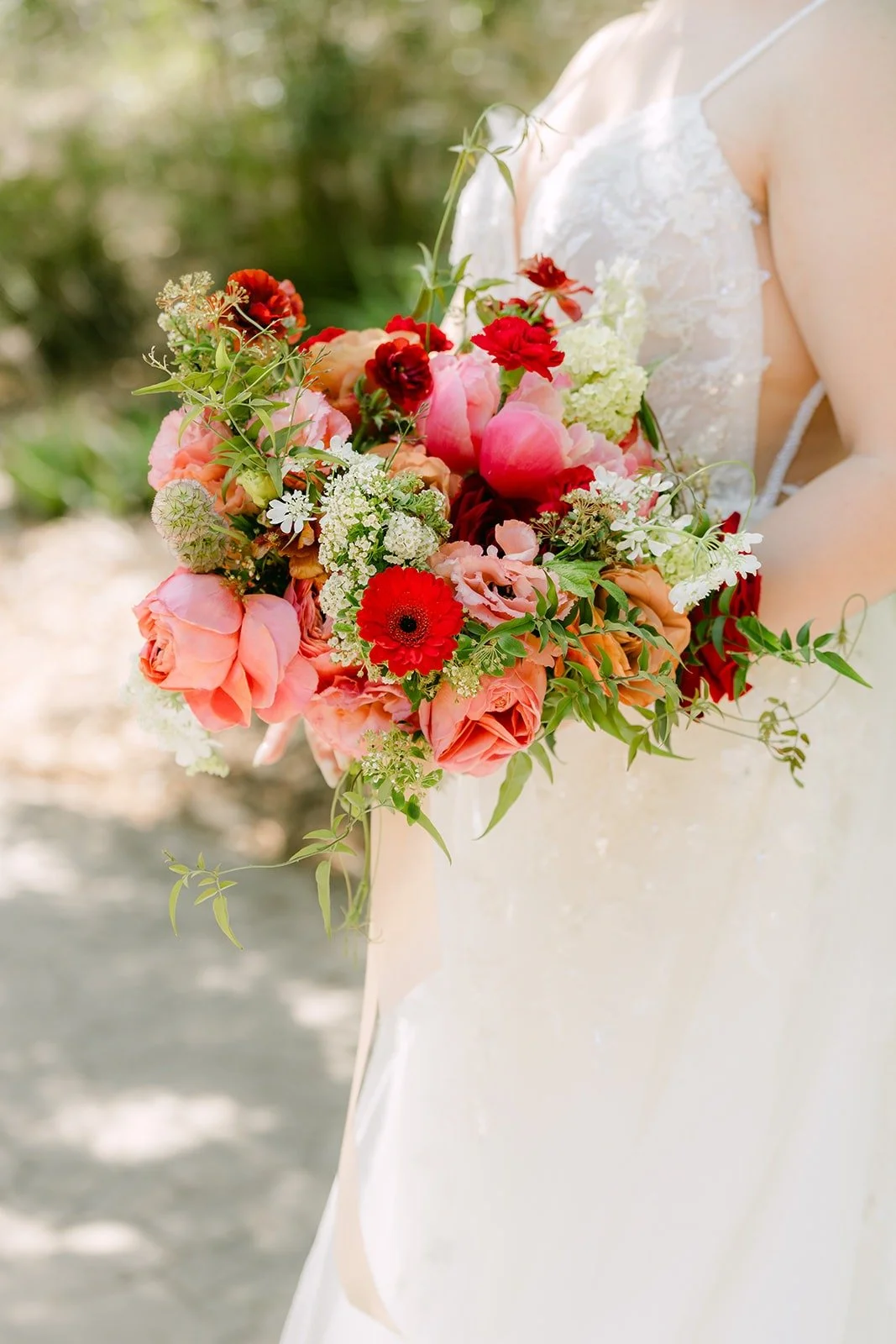 Joanne's red, pink and peach bouquet held against her lace gown