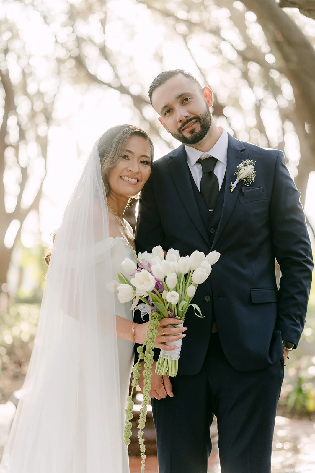 Mariana holding white tulips beside Danny under the olive branches