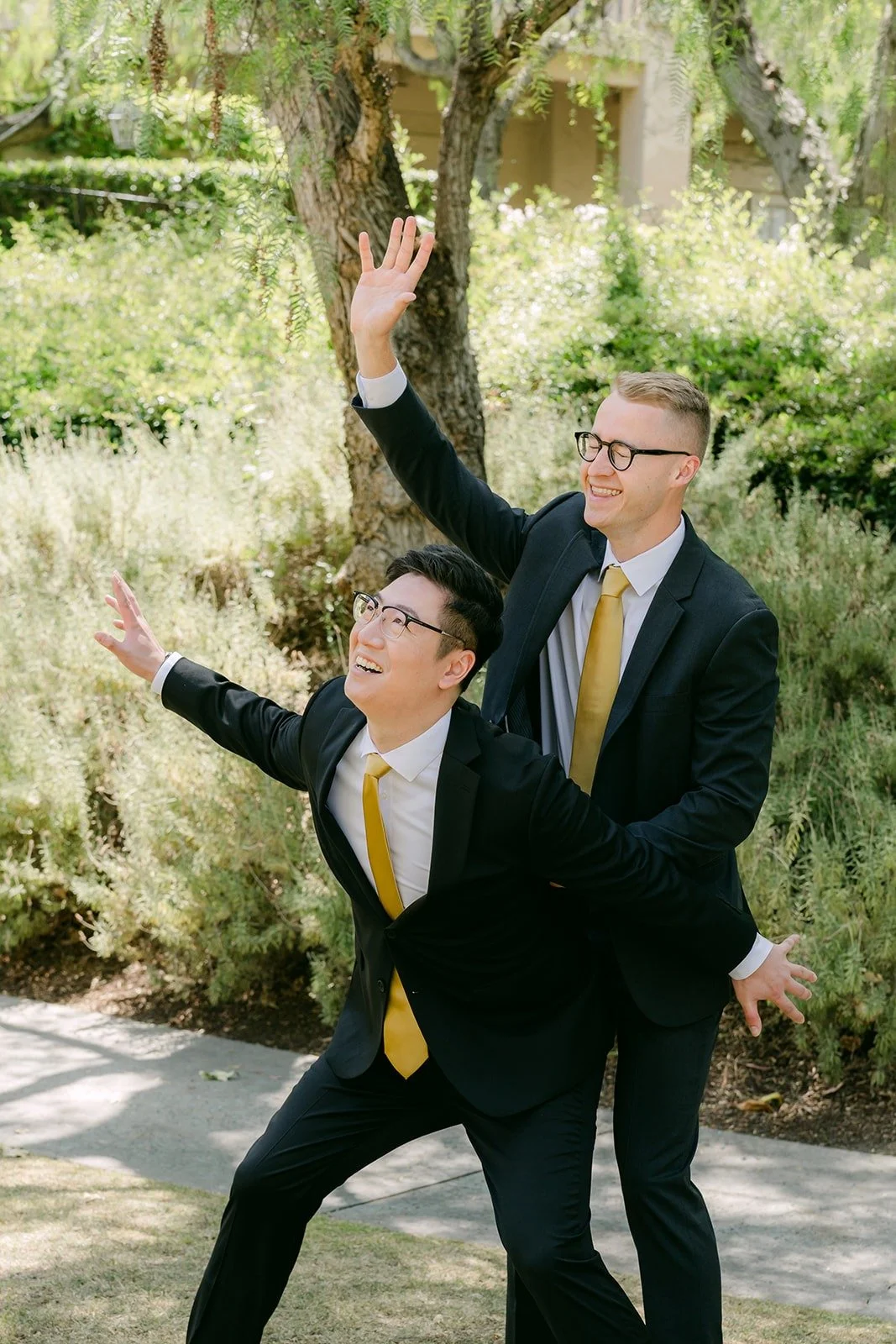 A groomsman leaping into a catch pose next to Zach in the garden