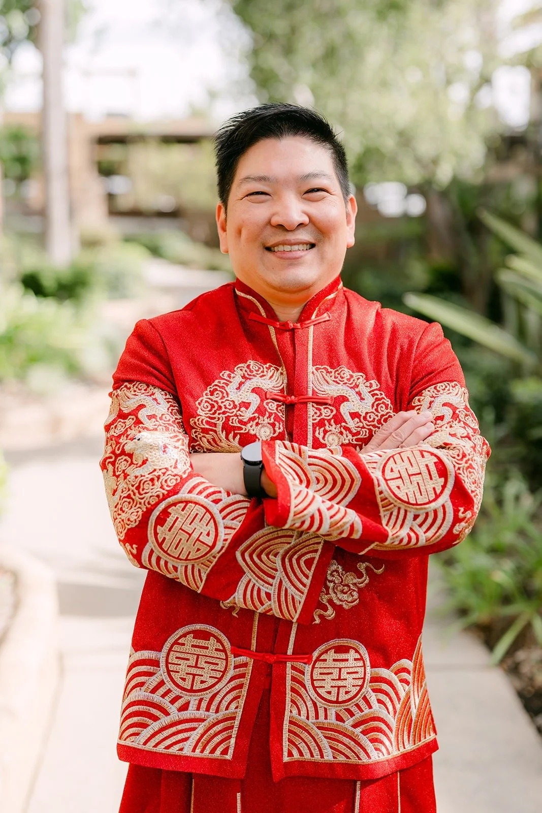 Jay smiles with his arms crossed in his red and gold jacket, photographed by One and Only Production