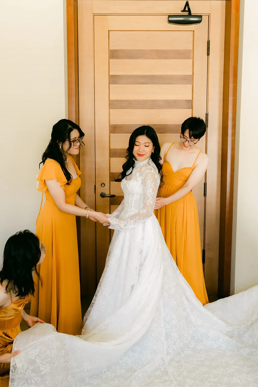 Bridesmaids in marigold helping Kim into her gown