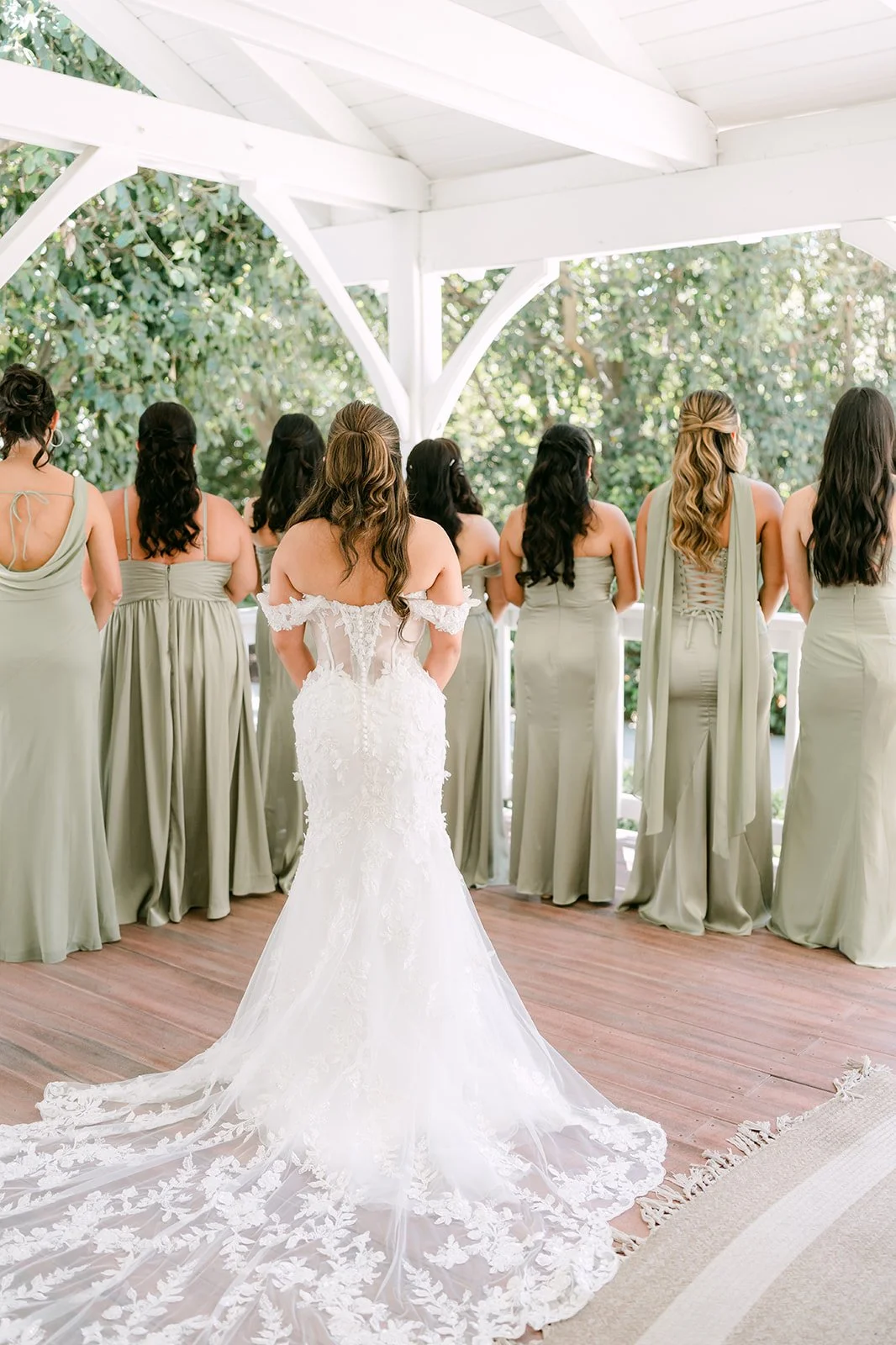 Nicole's bridesmaids in pistachio green gowns seeing her in her dress under the gazebo.