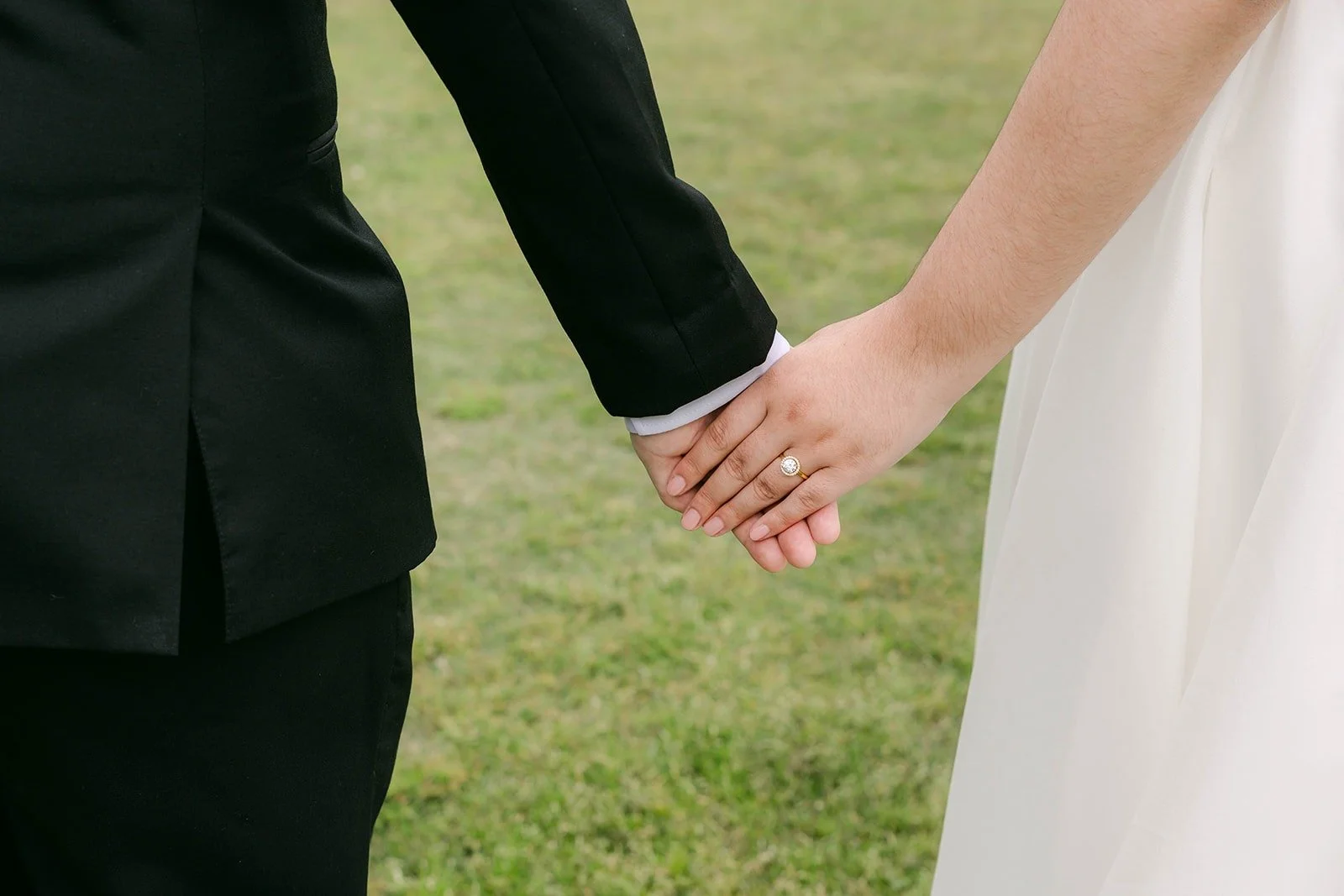 A close up of Saira and Matthew holding hands on the grass