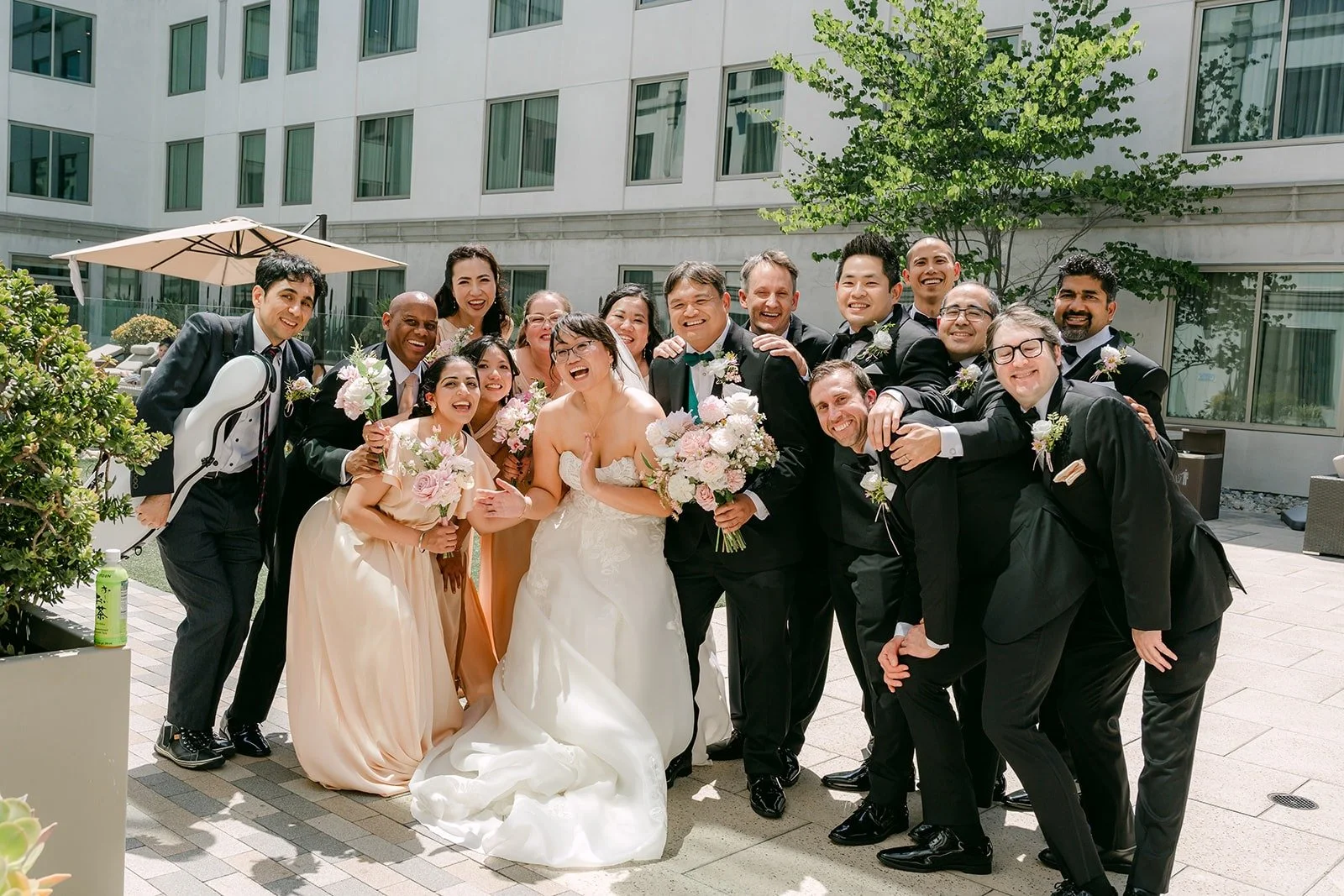 The wedding party crowding around Stella and James for a playful group photo, photographed by One and Only Production