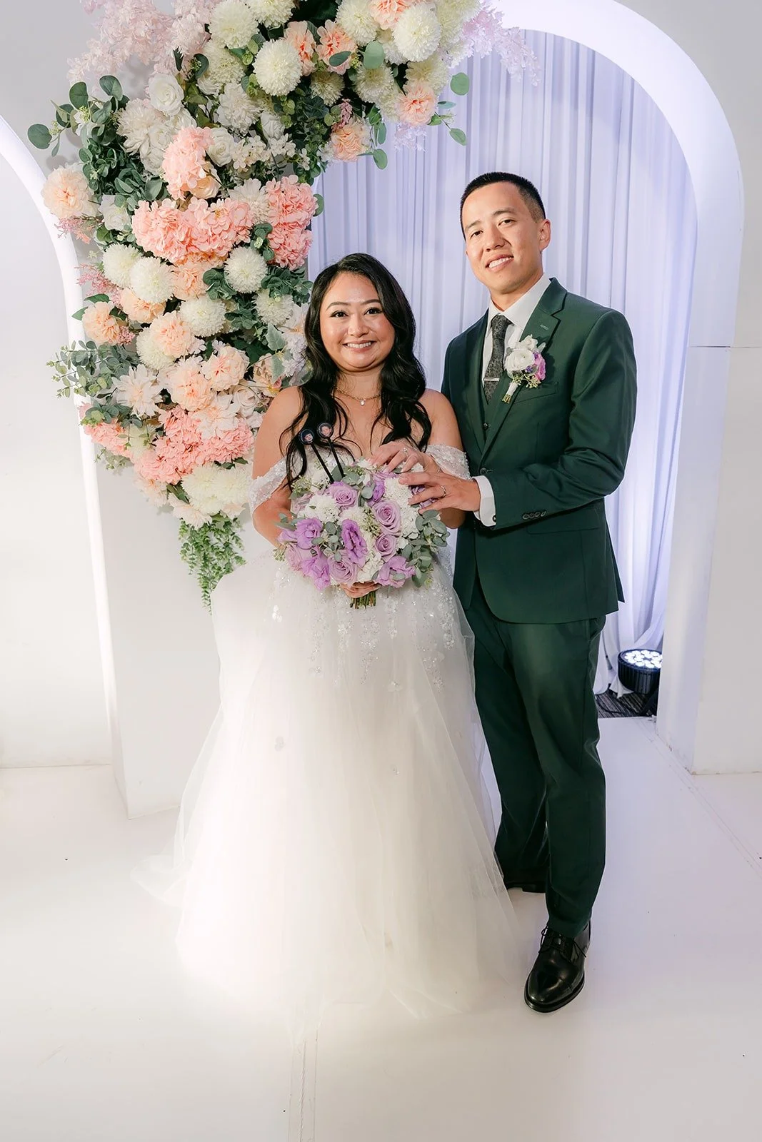 Jennifer and Kevin smile with her bouquet at the floral arch