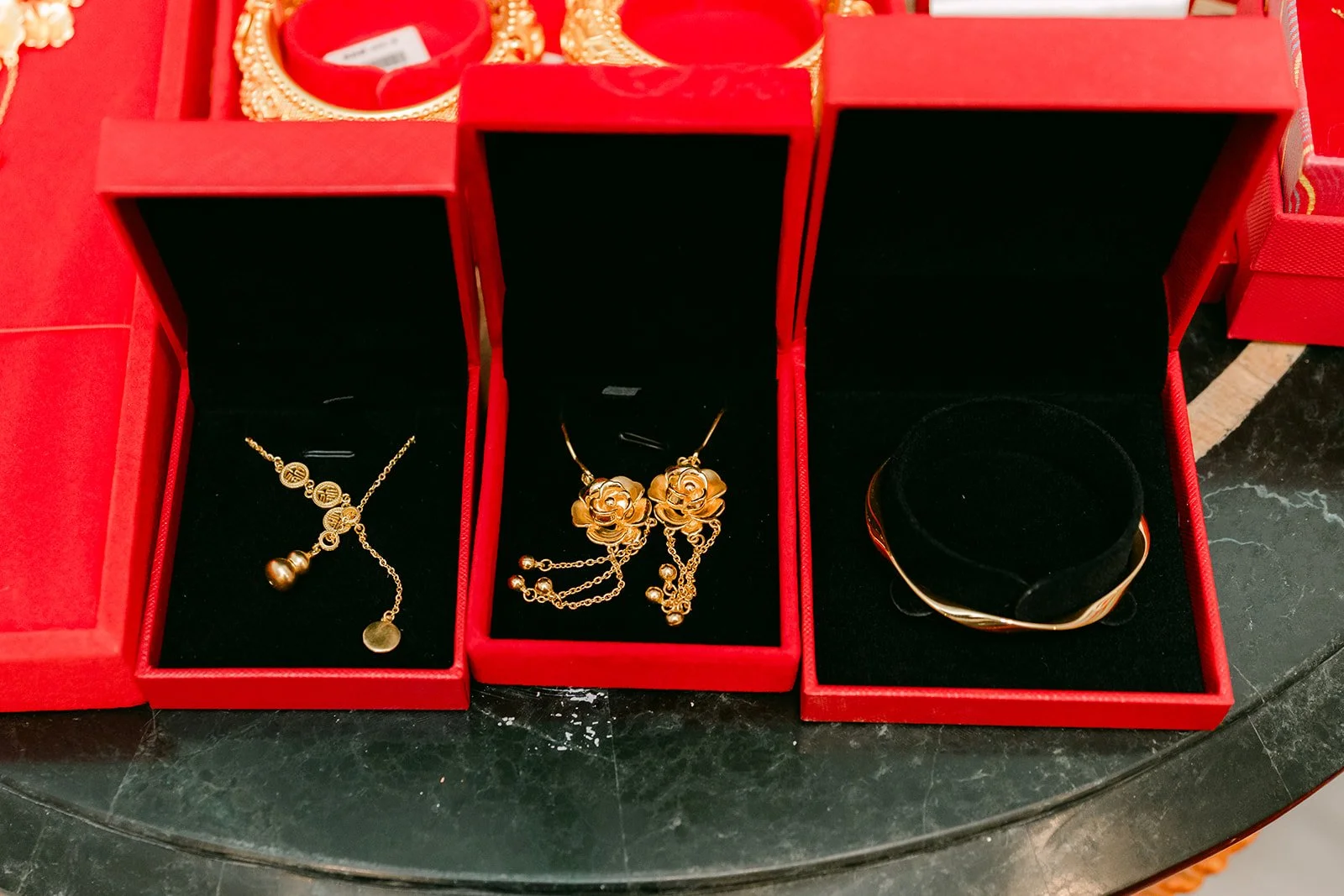 Three red jewelry boxes holding gold gifts for the bride.