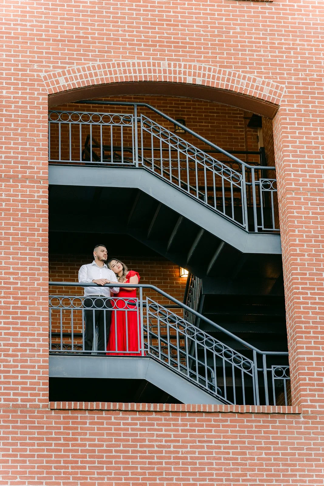 Linh and Ankush on a wrought iron stairway framed by a brick arch.