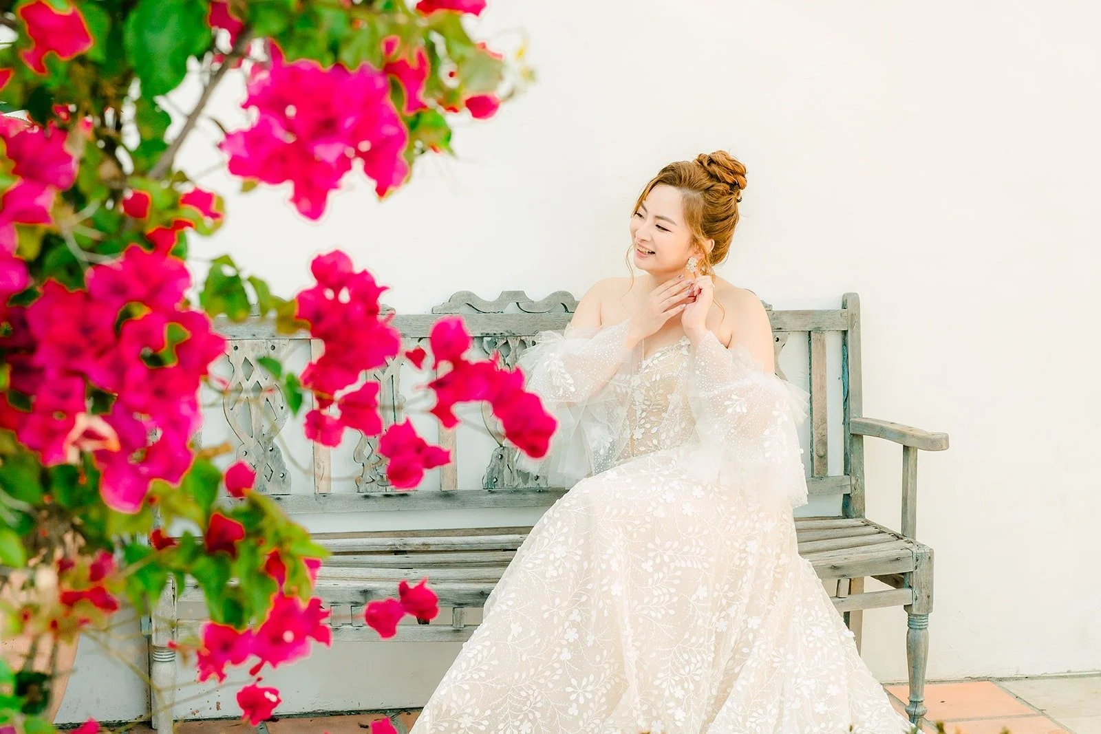 Joanna sitting on a courtyard bench beneath bright pink bougainvillea