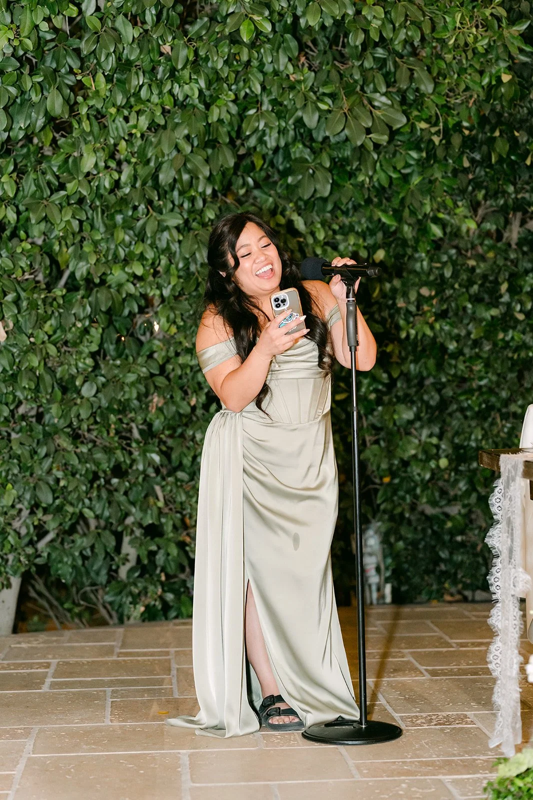 A maid of honor giving her toast against the ivy wall.
