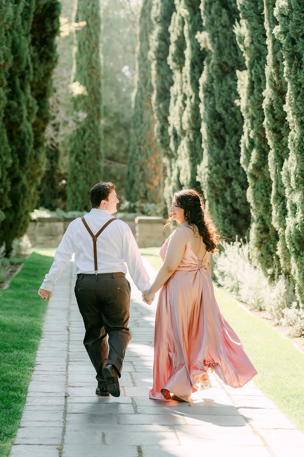 Saira and Matthew walking hand in hand down the cypress-lined path.