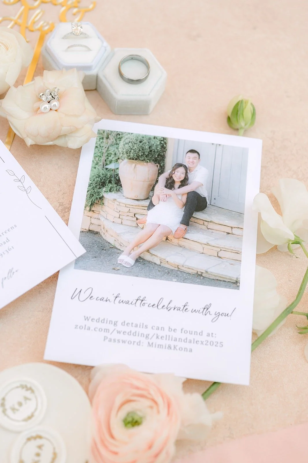 An engagement photo card of Kelli and Alex framed by ivory roses and ring boxes