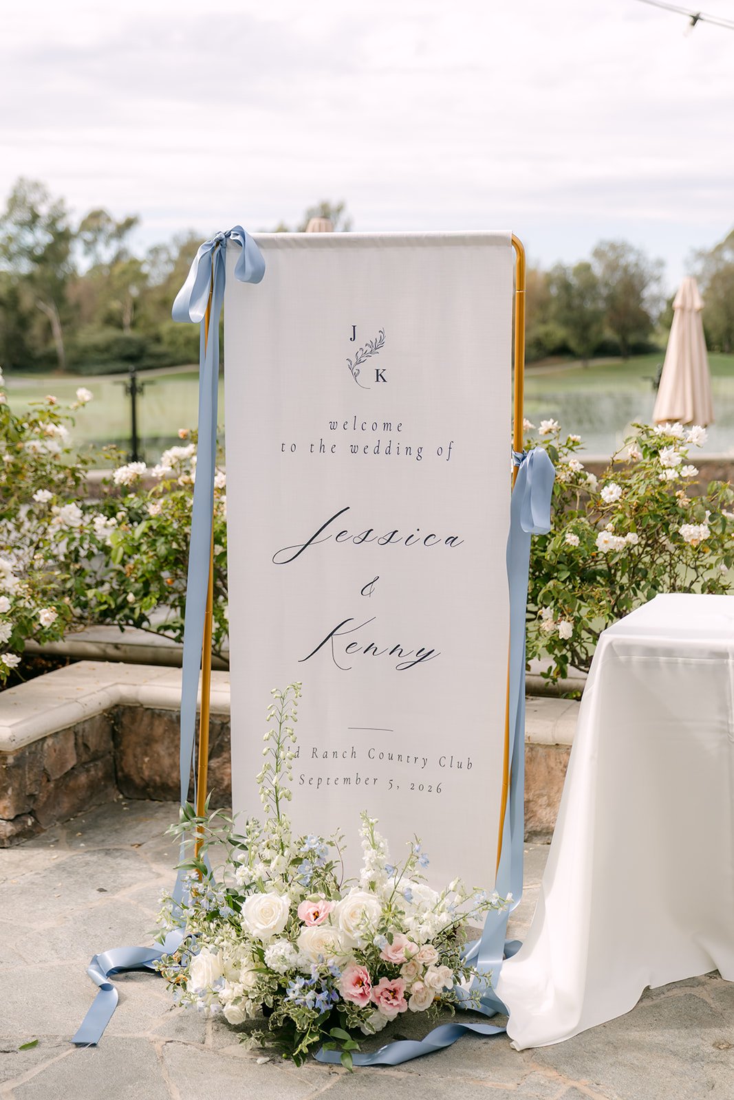 Jessica and Kenny's welcome sign with dusty blue ribbons and florals at Old Ranch Country Club