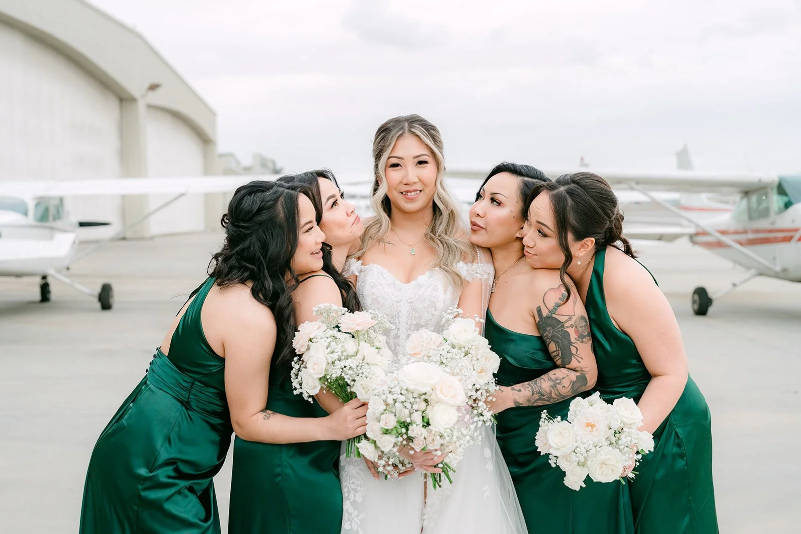 Bridesmaids hugging Raine in front of small airplanes