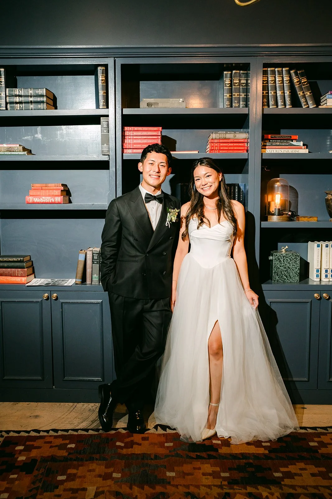 Jadee and Richard in front of the dark bookshelves, photographed by One and Only Production