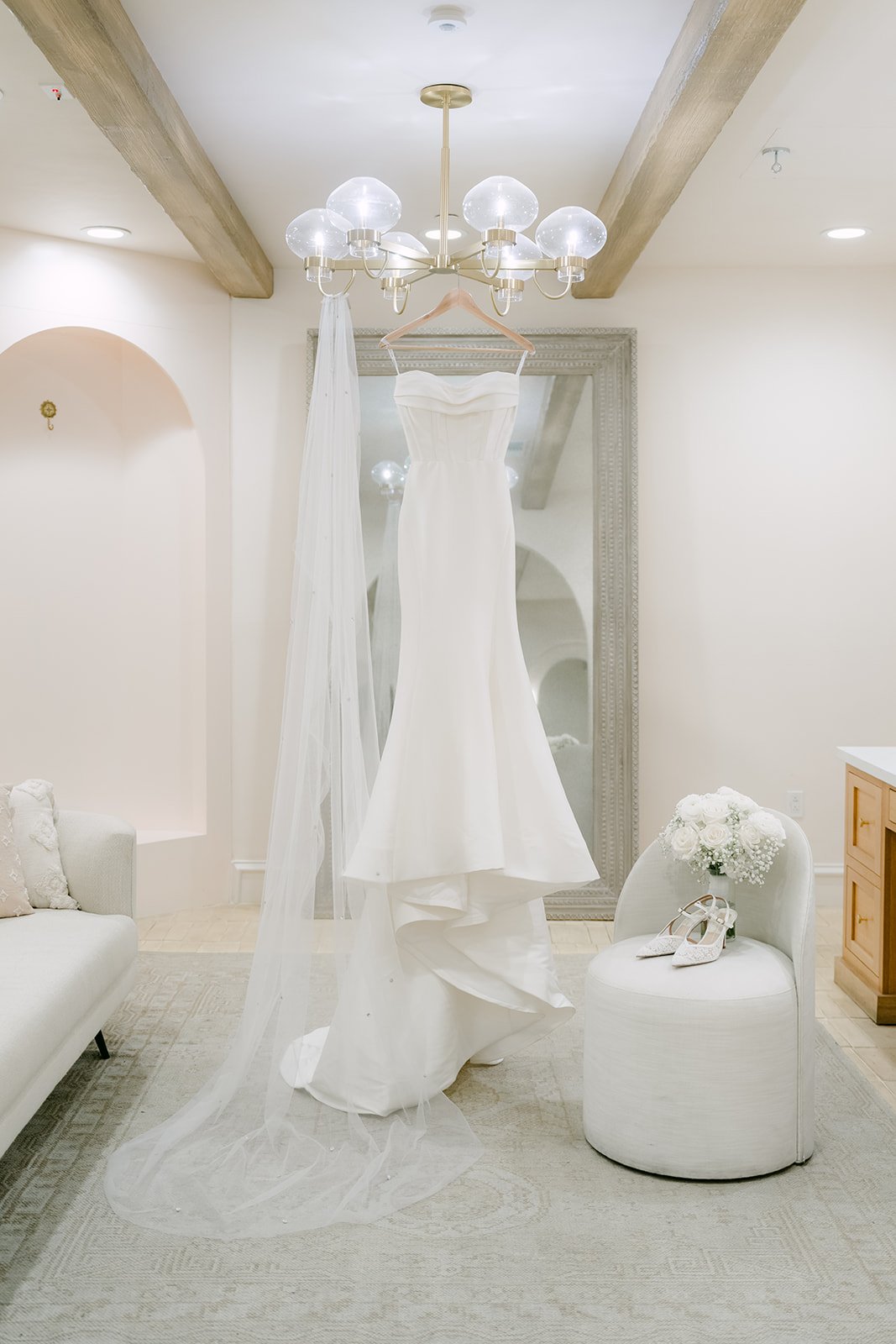 Strapless mermaid wedding gown and cathedral veil hanging from a chandelier in the bridal suite at Serra Plaza