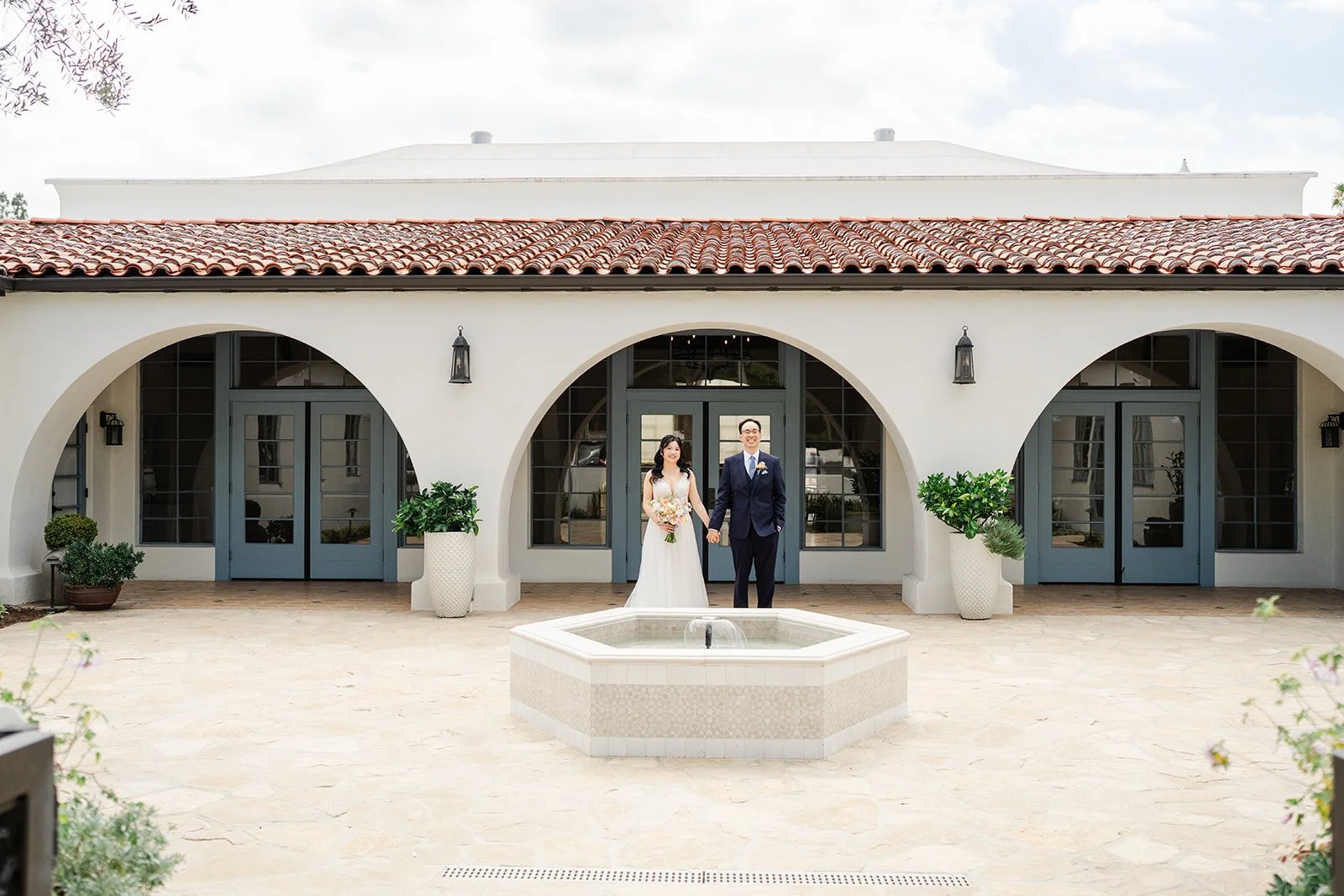 Wide view of the couple in the arched courtyard with its tile roof