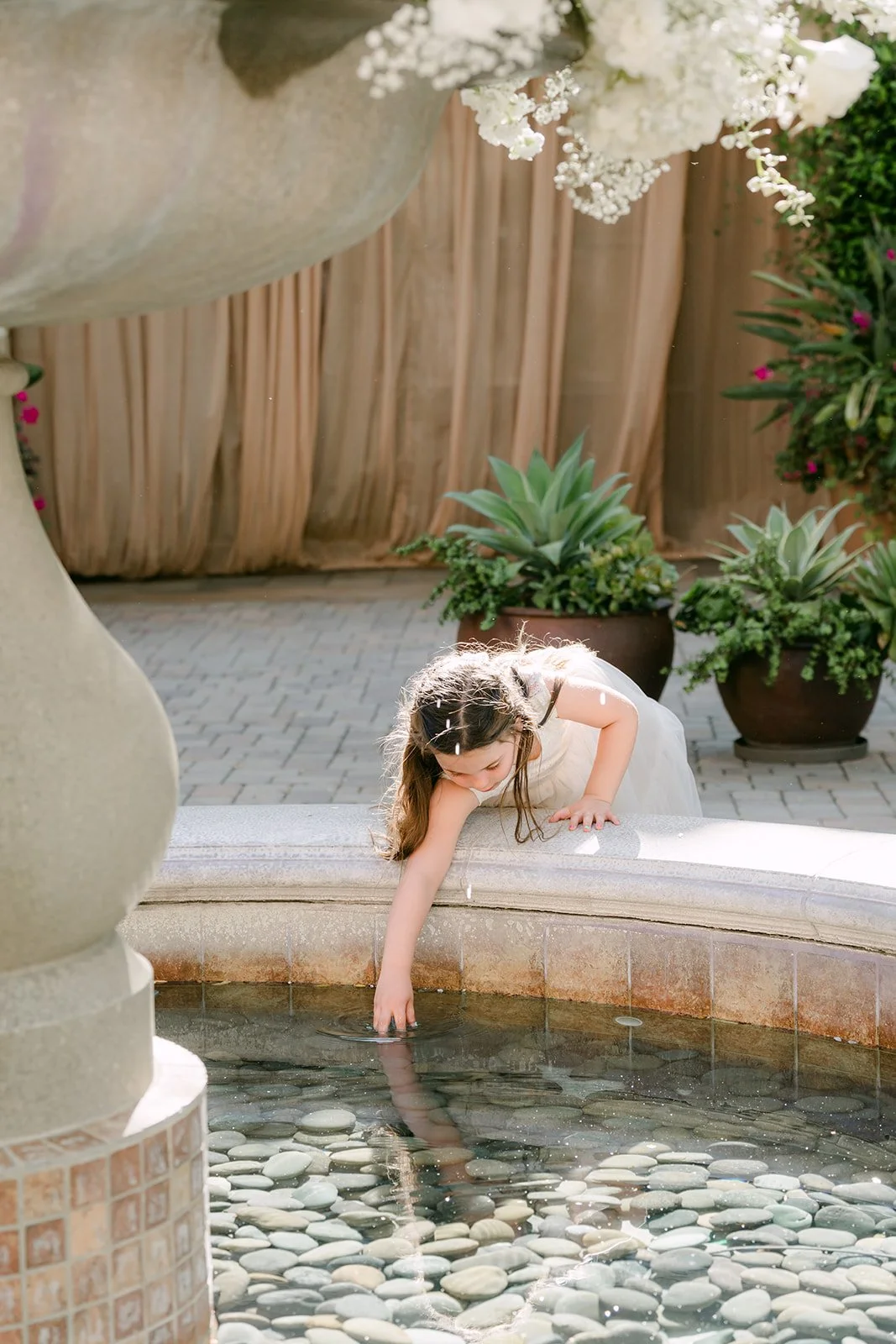 Flower girl reaching into the courtyard fountain during cocktail hour