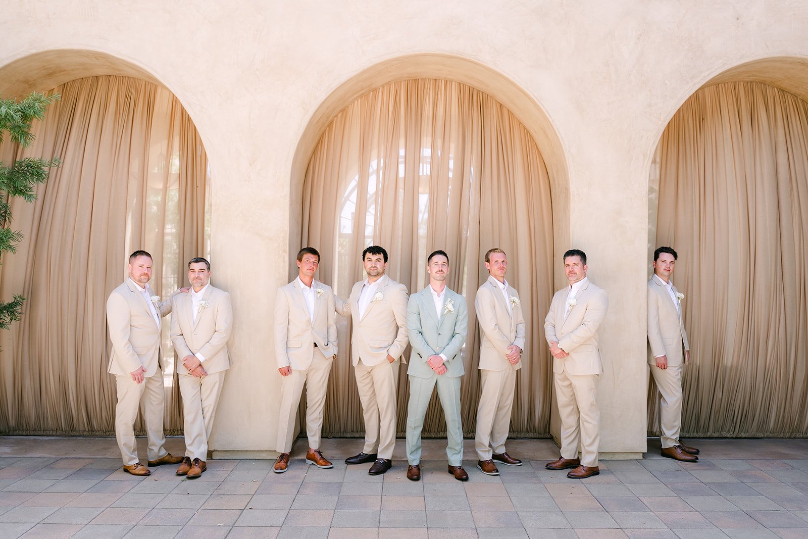 Groomsmen standing in a row beneath the arches at Serra Plaza
