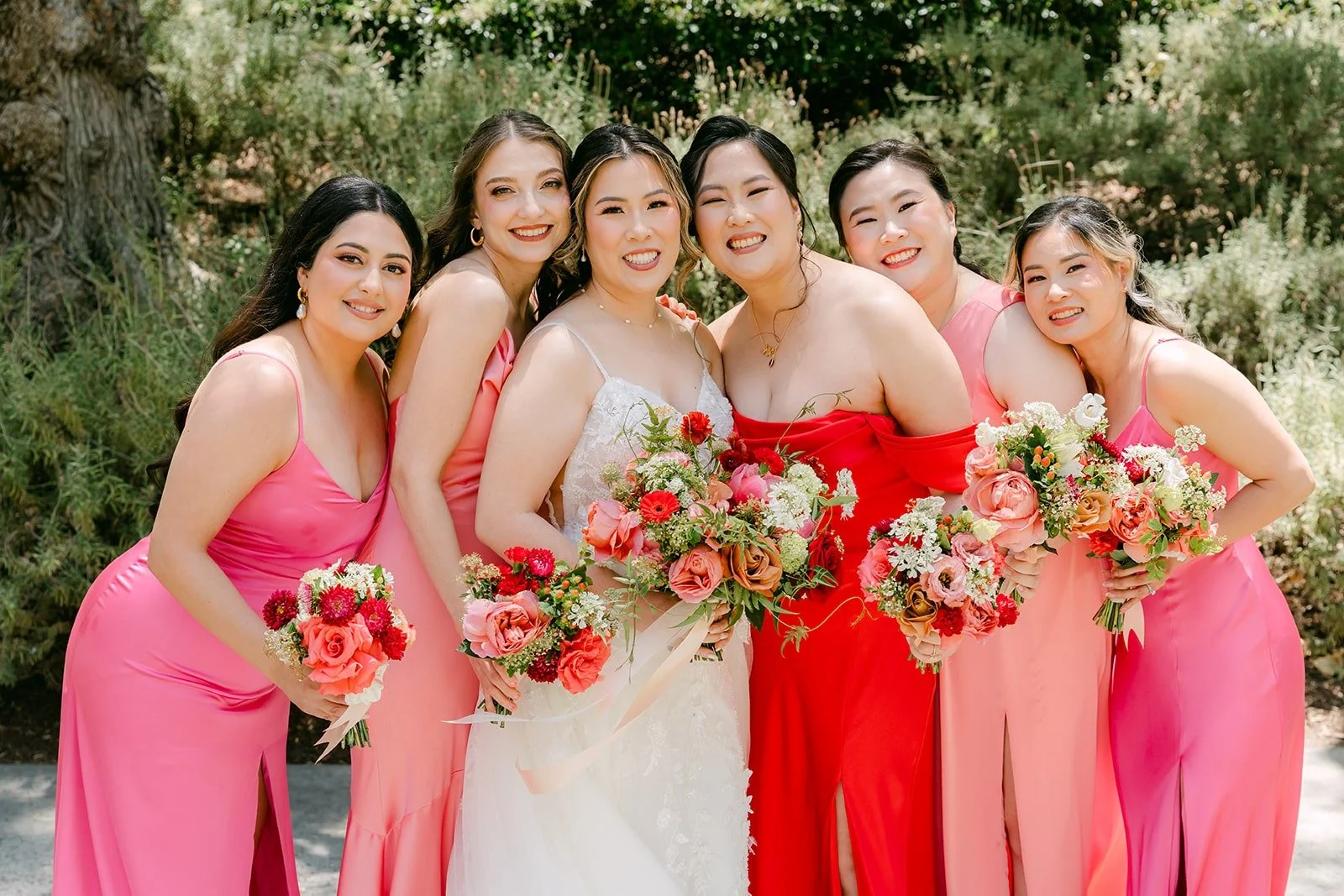 Joanne and her bridesmaids in shades of pink and red holding their bouquets in the garden