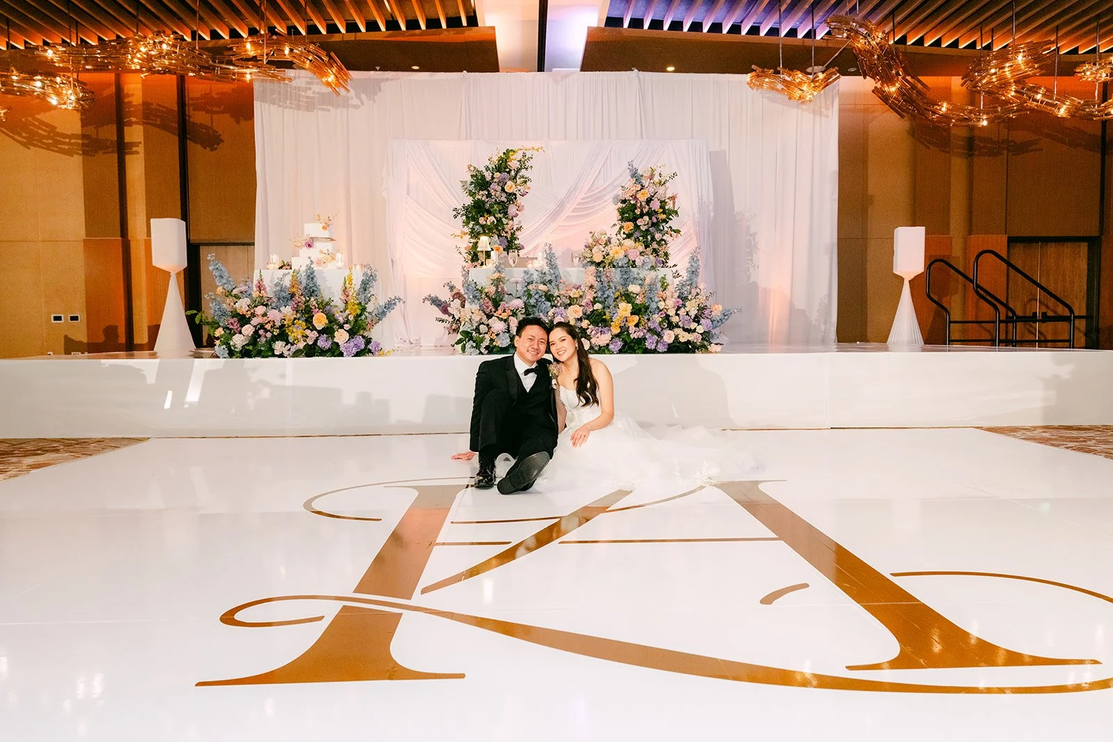 Couple sitting on the dance floor in front of their floral backdrop