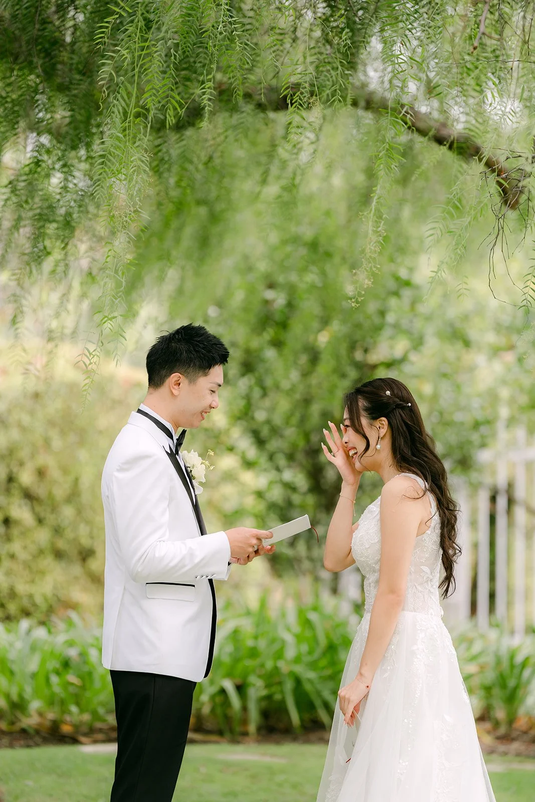 Ryan reading his vows as Jenny wipes away a tear under a willow tree.