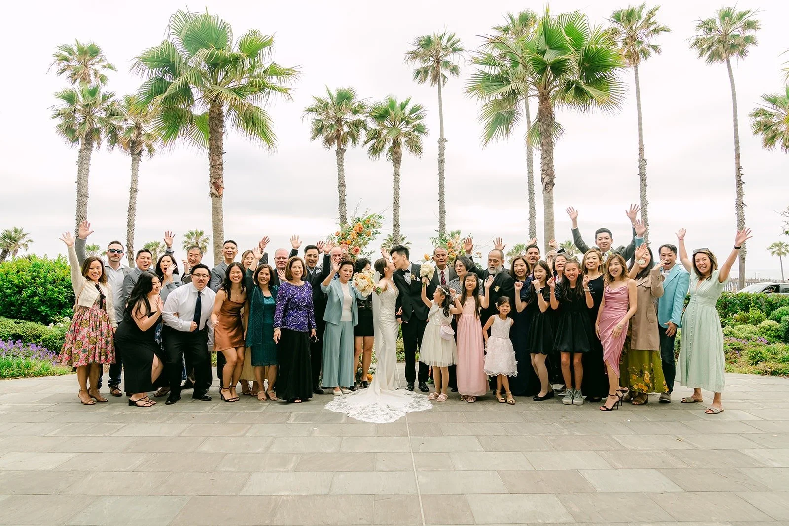 Angela and Eli with all of their guests in a big group photo on the terrace, palms behind
