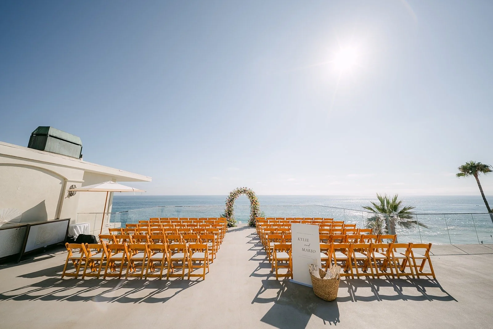 The ceremony set on the oceanfront terrace with wooden chairs facing a floral arch