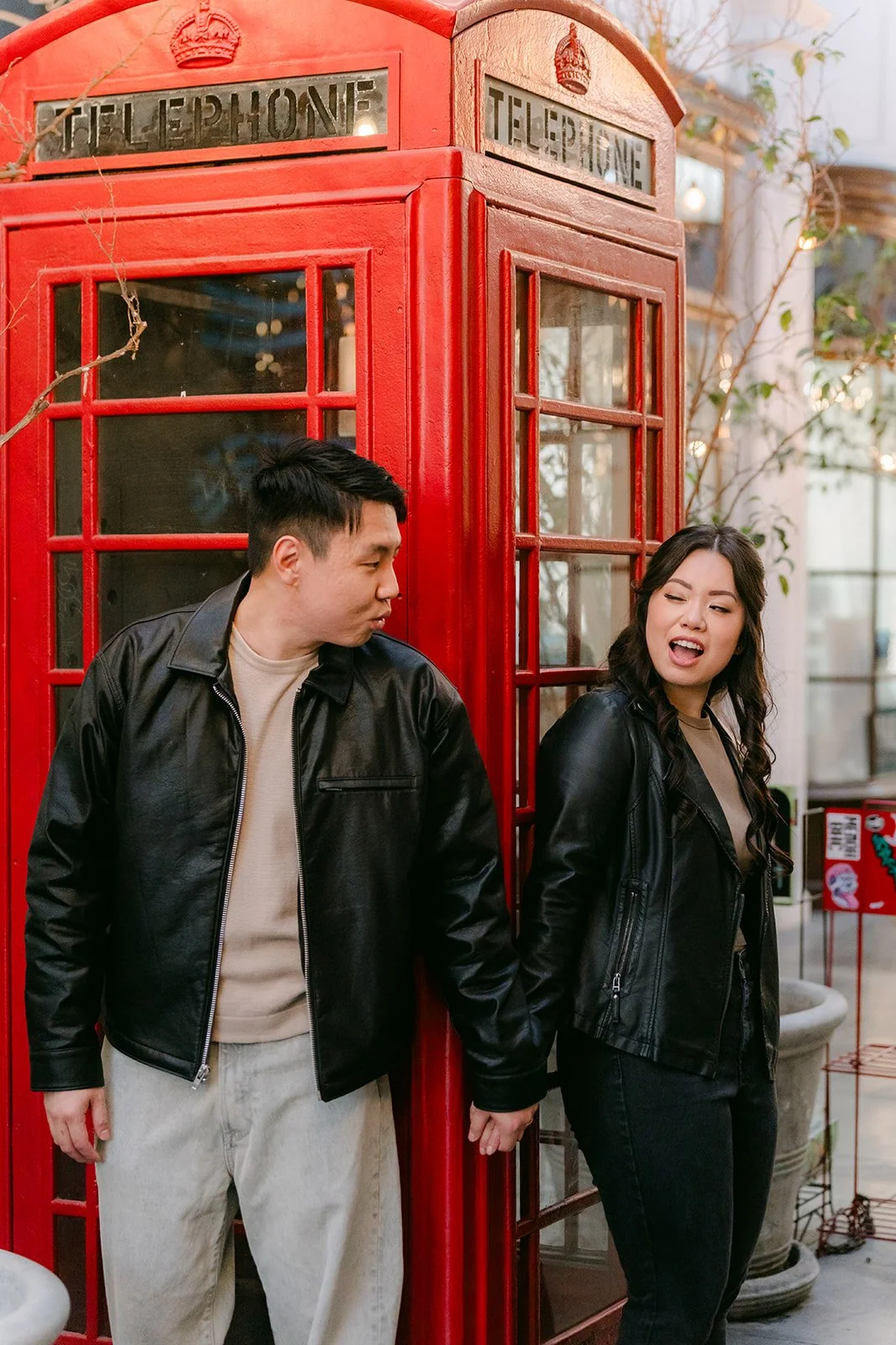 Emily and James stand side by side next to the red phone booth.