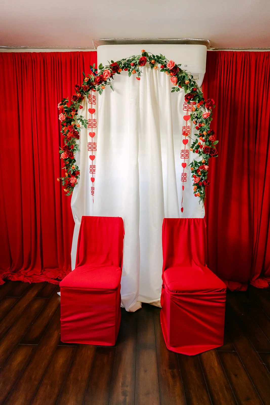 Tea ceremony setup with red chairs, a rose arch and red curtains.