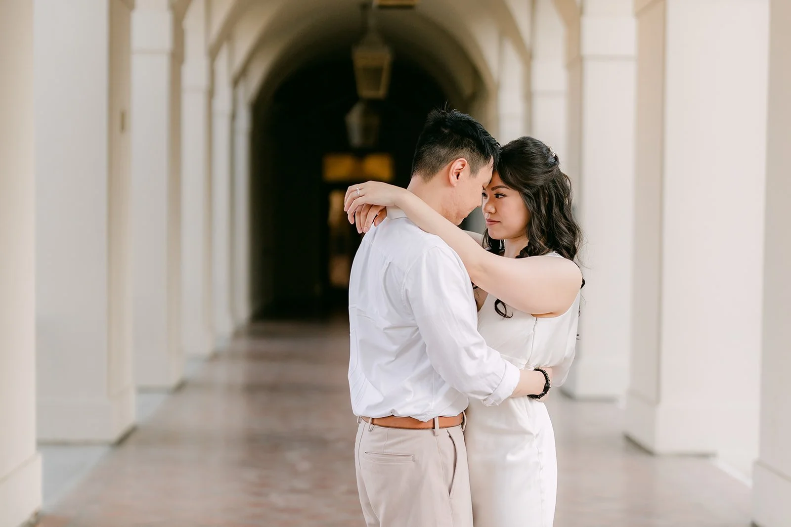 Emily and James embrace inside the arched walkway with soft light behind them.