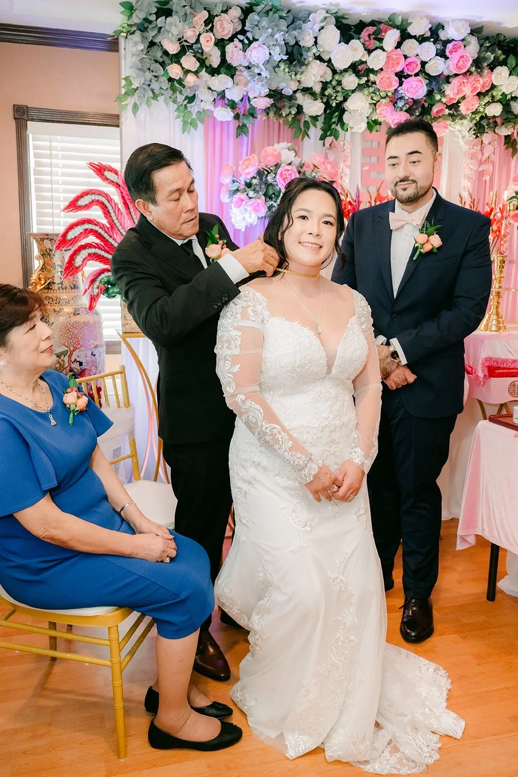 A relative fastening a gold necklace on Amy as James stands beside her