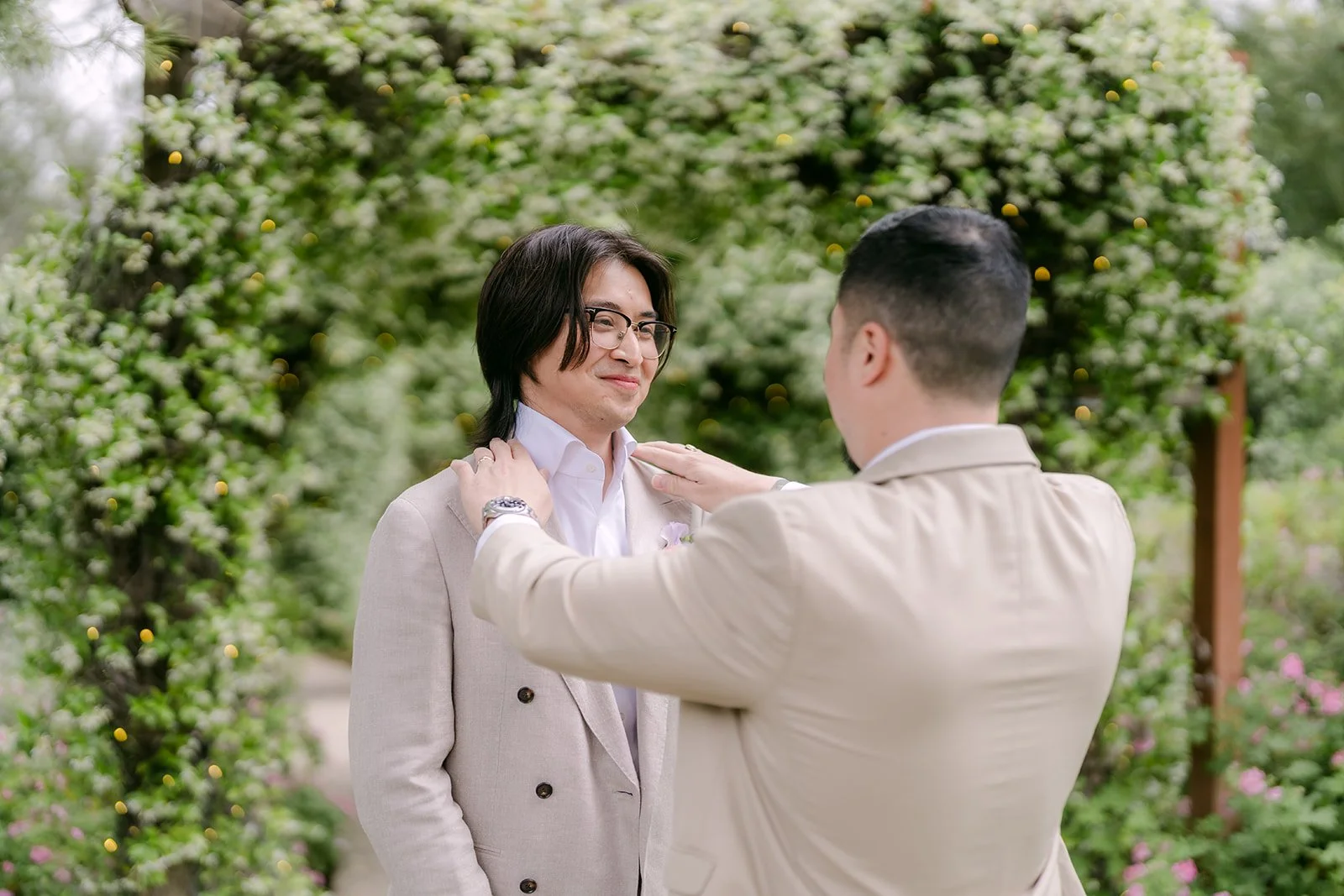 Groomsman straightening Mike's jacket under an ivy covered arch