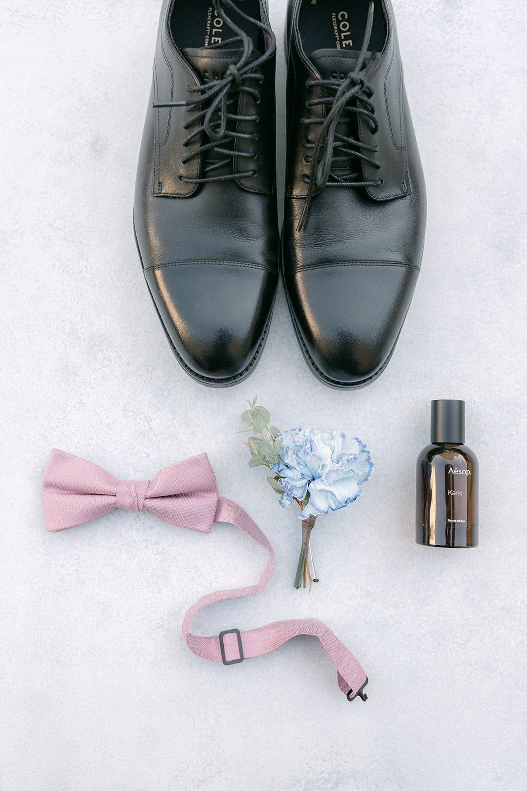 Brandon's black dress shoes, pink bow tie, suspenders and blue boutonniere in a flat lay