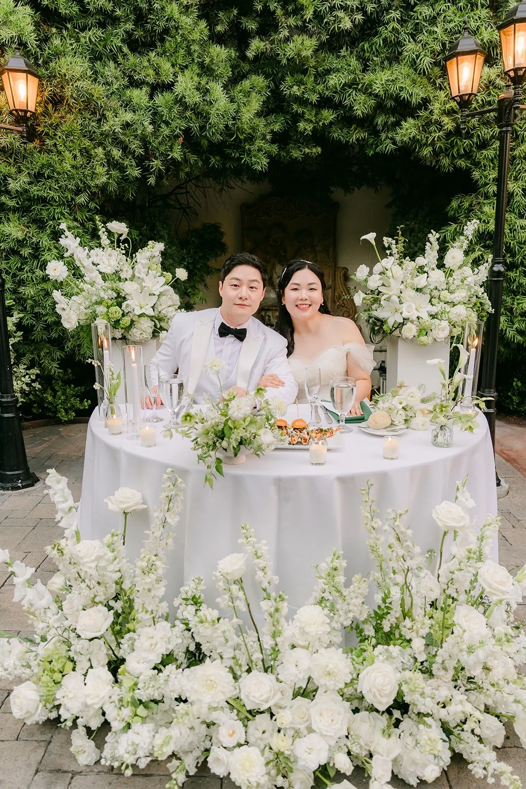 Chorok and Min Soo at their sweetheart table surrounded by white florals, photographed by One and Only Production