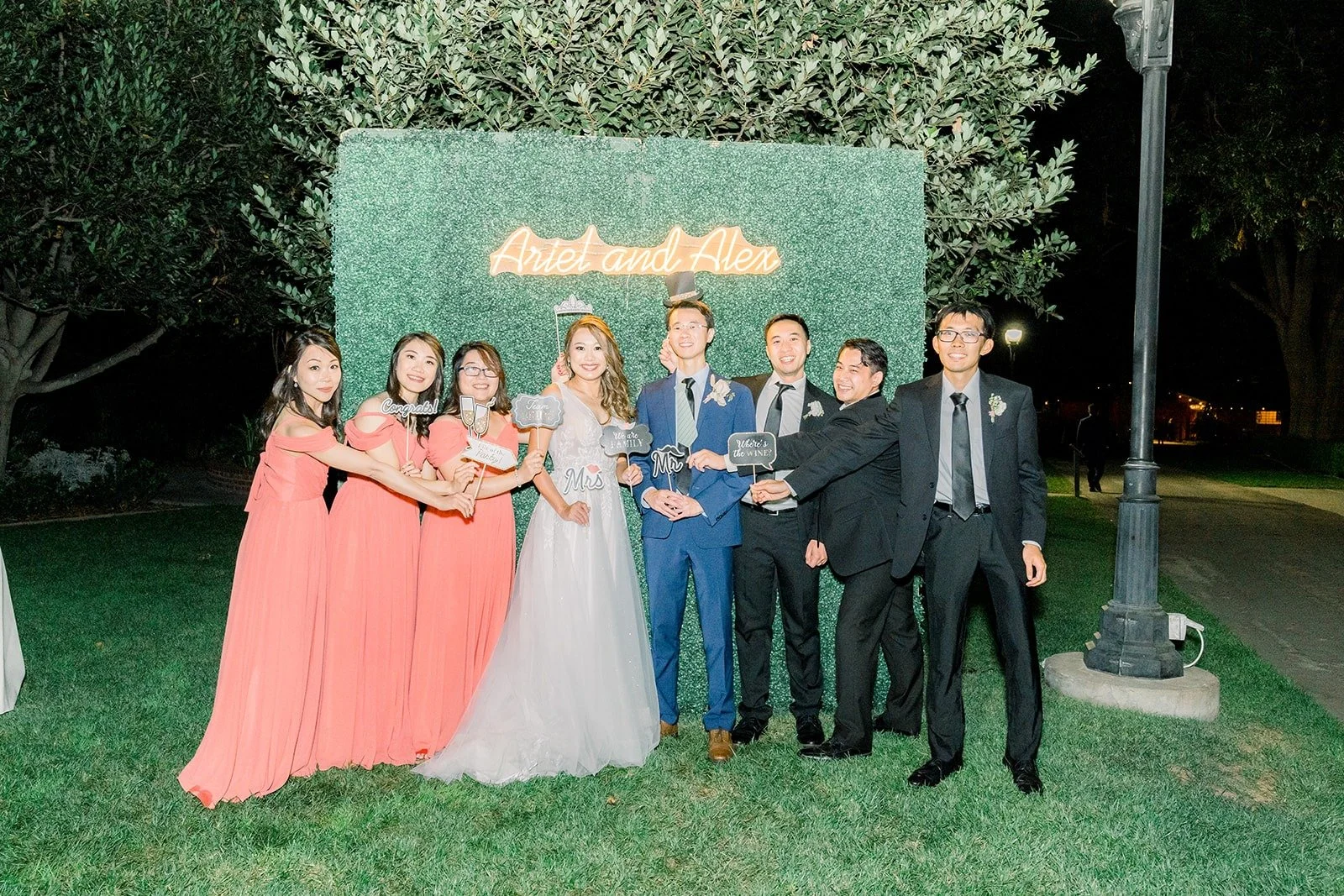 The wedding party in front of a greenery wall, photographed by One and Only Production