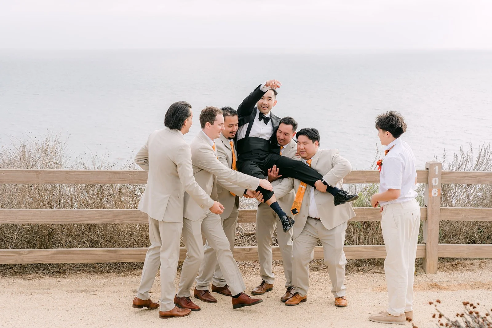 Groomsmen goofing around by the wooden fence above the Pacific