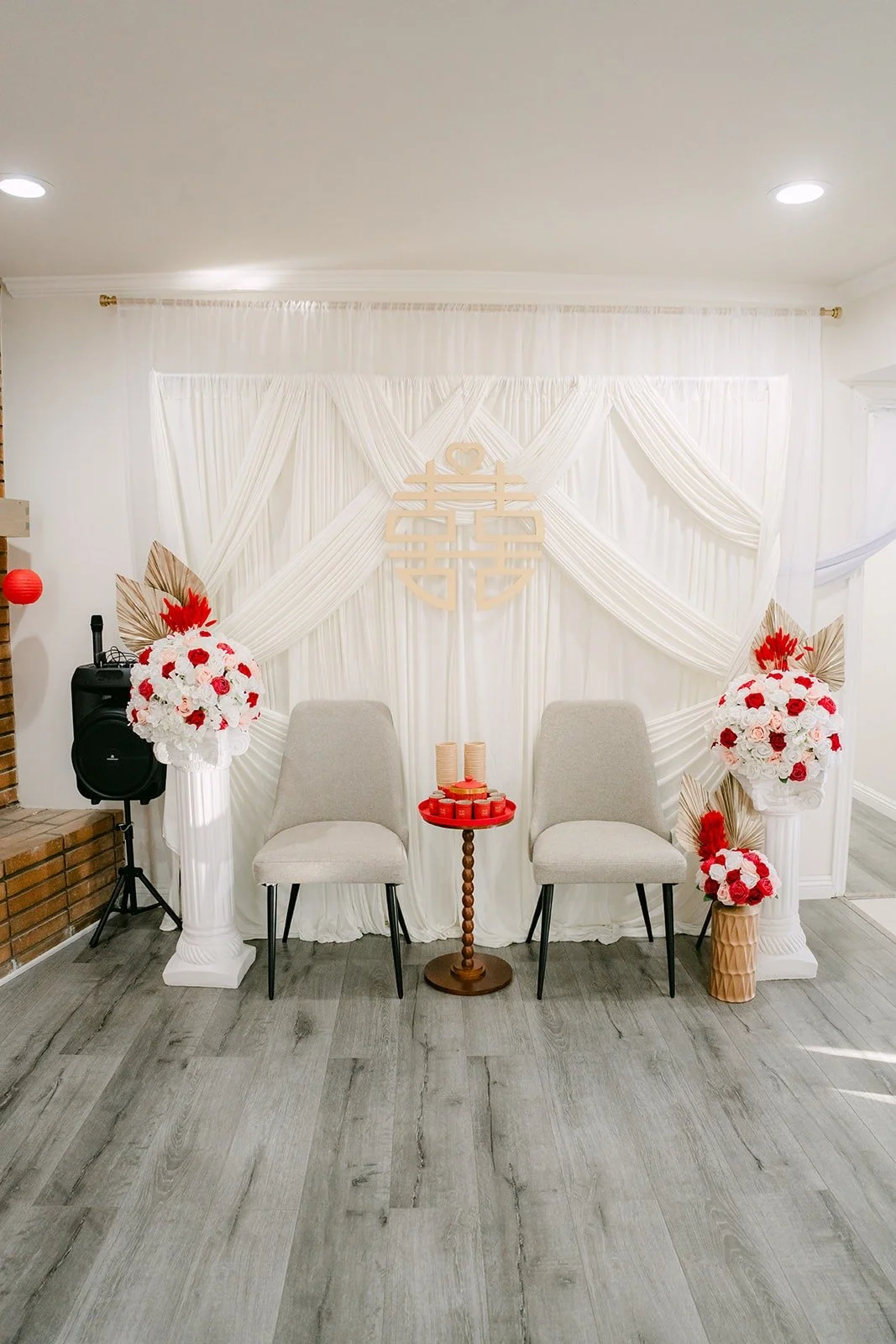 The tea ceremony room at home, with white draping, a red double happiness symbol and red and white floral columns