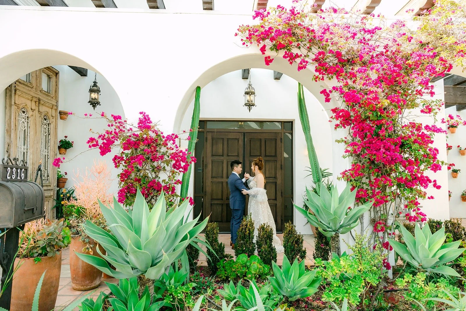 Joanna and Jerrick beneath the white arch with pink bougainvillea spilling over it