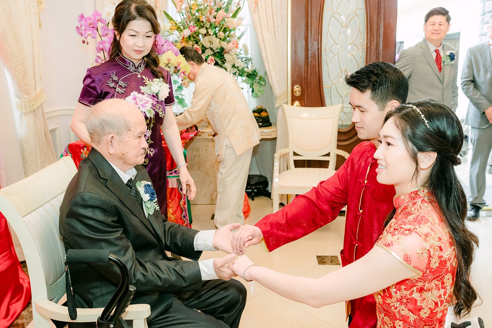 The couple holding an elder's hands as he gives his blessing.
