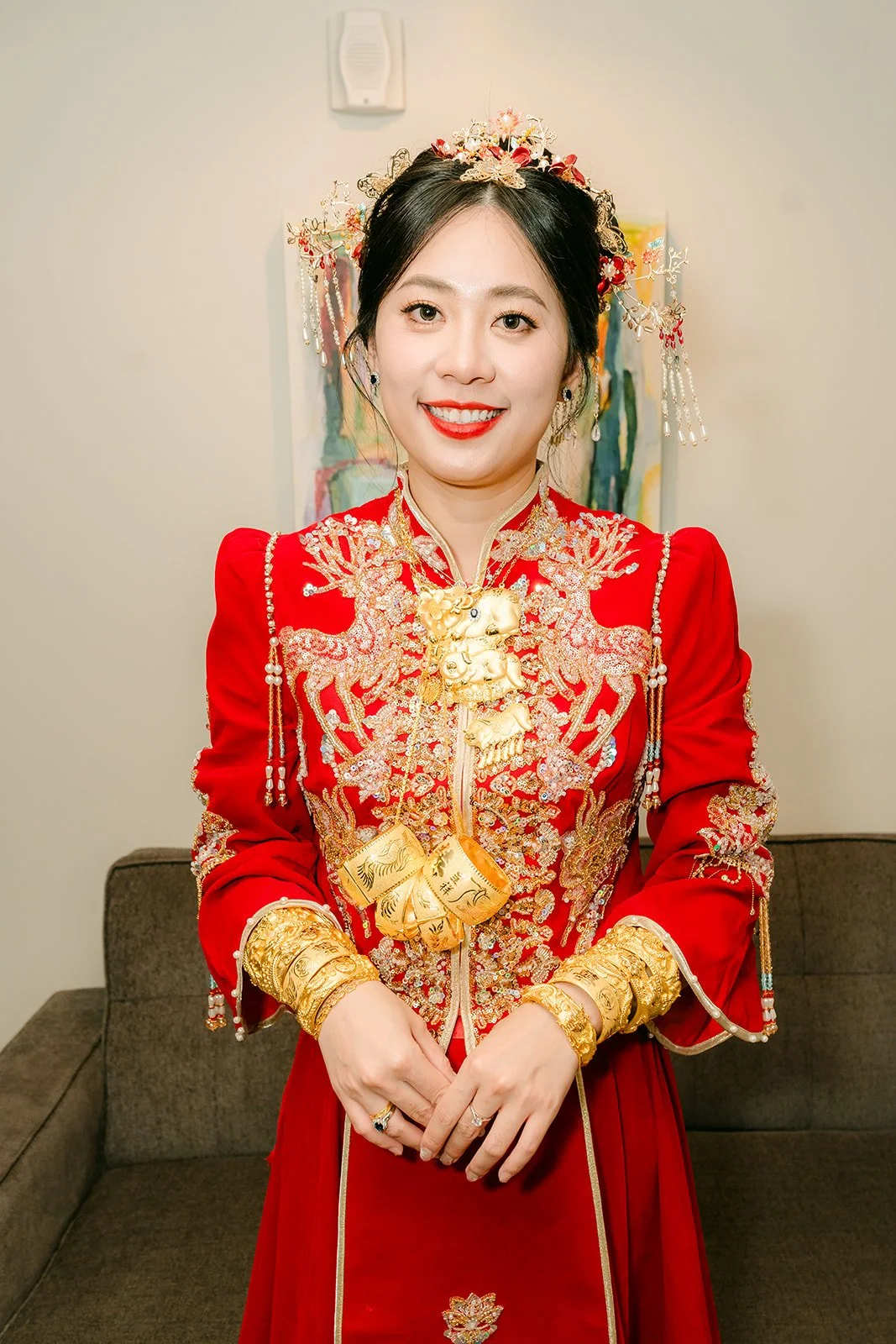 A bride in a full gold embroidered qun kwa and gold headpiece seated on the sofa.